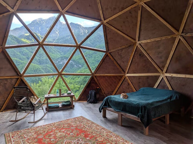 Inside the dome — a triangulated glass wall framing the mountains, a double bed and a traditional Armenian rug